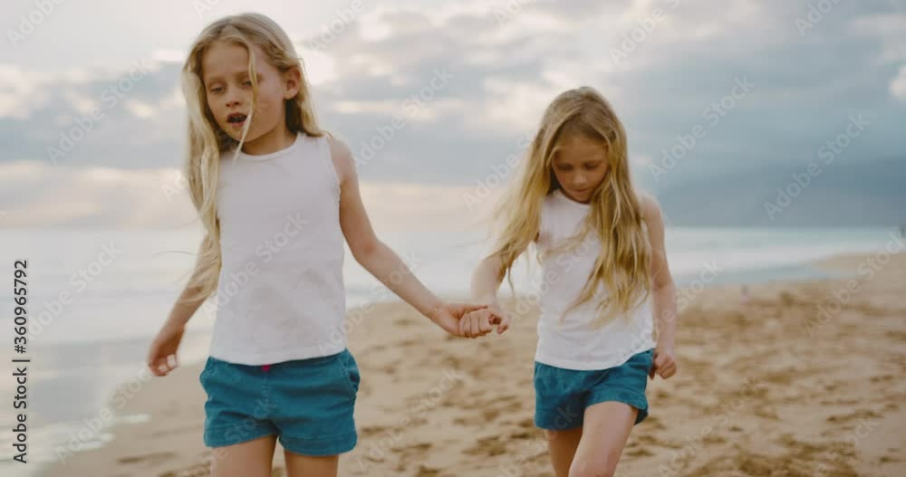 Happy young twin girls walking down the beach playing at sunset, summer family lifestyle Happy young twin girls walking down the beach playing at sunset, summer family lifestyle