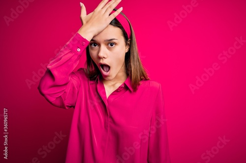 Young beautiful brunette girl wearing casual shirt standing over isolated pink background surprised with hand on head for mistake, remember error. Forgot, bad memory concept.