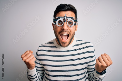 Young handsome man with beard wearing optometry glasses over isolated white background celebrating surprised and amazed for success with arms raised and open eyes. Winner concept.