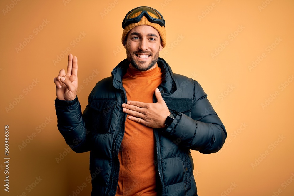 Young handsome skier man with beard wearing snow sportswear and ski goggles smiling swearing with hand on chest and fingers up, making a loyalty promise oath Young handsome skier man with beard wearing snow sportswear and ski goggles smiling swearing with hand on chest and fingers up, making a loyalty promise oath