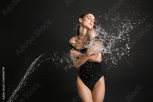 Beautiful young woman and splash of water on dark background