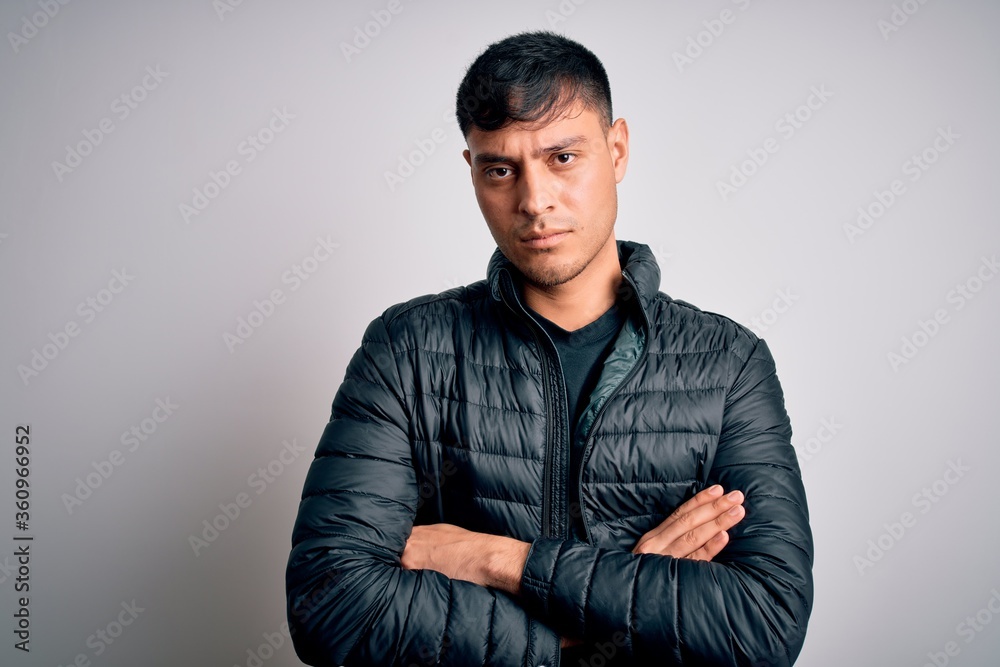 Young handsome hispanic man wearing winter coat standing over white isolated background skeptic and nervous, disapproving expression on face with crossed arms. Negative person.