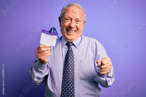 Senior grey haired business man holding identification tag over purple background screaming proud and celebrating victory and success very excited, cheering emotion