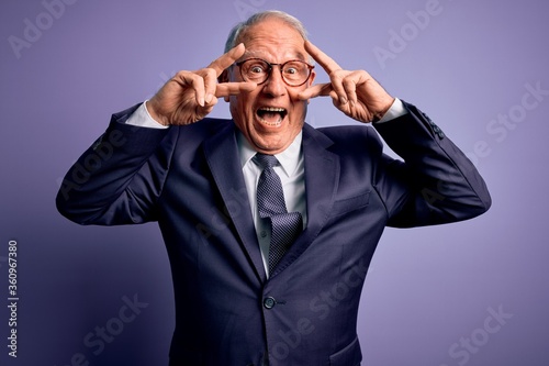 Grey haired senior business man wearing glasses and elegant suit and tie over purple background Doing peace symbol with fingers over face, smiling cheerful showing victory