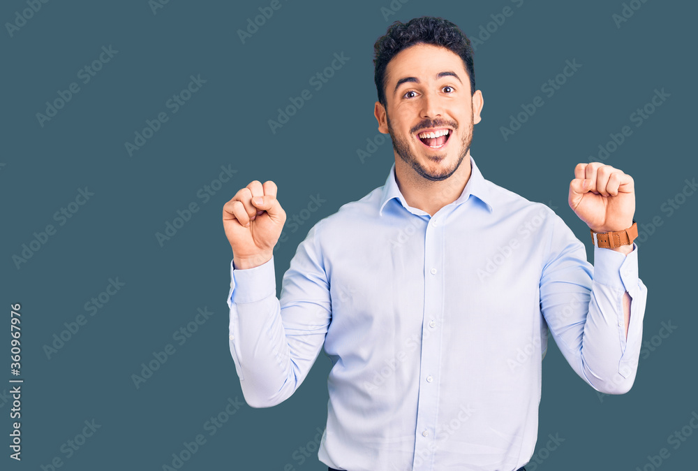 Young hispanic man wearing business clothes celebrating surprised and amazed for success with arms raised and open eyes. winner concept. Young hispanic man wearing business clothes celebrating surprised and amazed for success with arms raised and open eyes. winner concept.