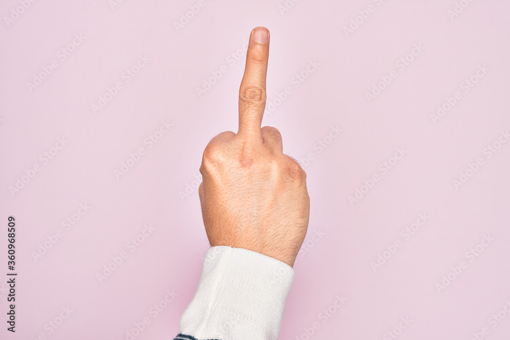 Hand of caucasian young man showing fingers over isolated pink background showing provocative and rude gesture doing fuck you symbol with middle finger