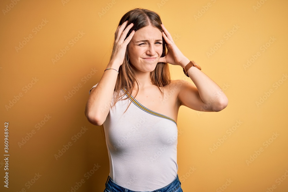 Fototapeta premium Young beautiful redhead woman wearing casual t-shirt over isolated yellow background suffering from headache desperate and stressed because pain and migraine. Hands on head.