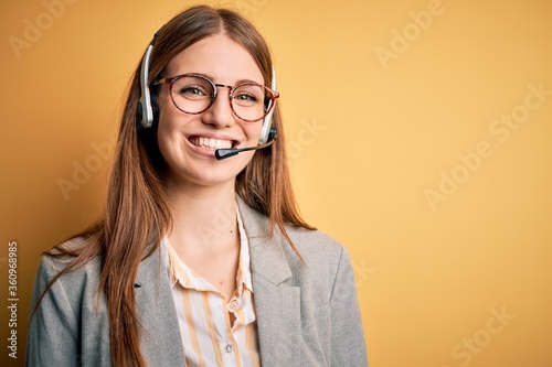 Young redhead call center agent woman overworked wearing glasses using headset with a happy and cool smile on face. Lucky person. photo