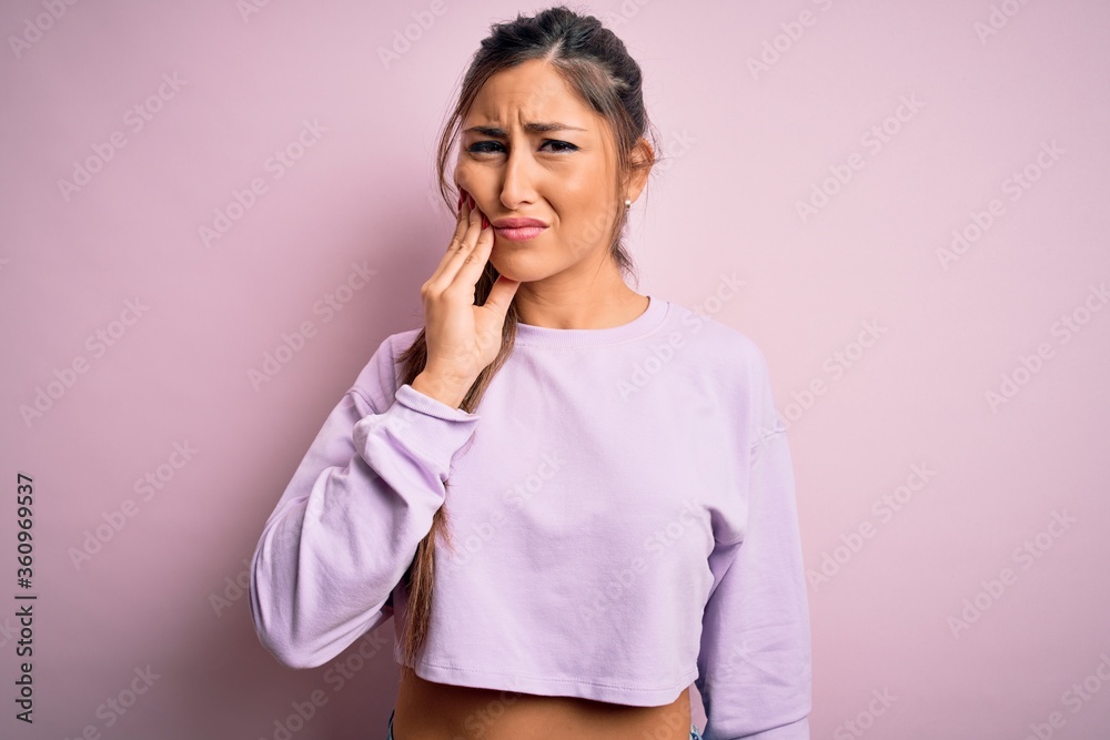 Young beautiful sport woman wearing sweatshirt over pink isolated background touching mouth with hand with painful expression because of toothache or dental illness on teeth. Dentist Young beautiful sport woman wearing sweatshirt over pink isolated background touching mouth with hand with painful expression because of toothache or dental illness on teeth. Dentist