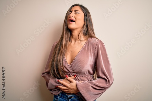 Young beautiful brunette elegant woman with long hair standing over isolated background with hand on stomach because nausea, painful disease feeling unwell. Ache concept.