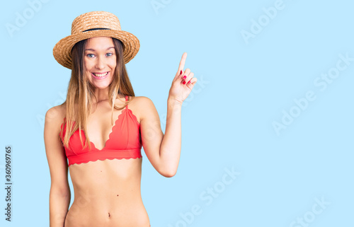 Beautiful brunette young woman wearing bikini showing and pointing up with finger number one while smiling confident and happy.