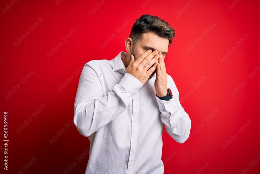 Young business man with blue eyes wearing elegant shirt standing over red isolated background rubbing eyes for fatigue and headache, sleepy and tired expression. Vision problem Young business man with blue eyes wearing elegant shirt standing over red isolated background rubbing eyes for fatigue and headache, sleepy and tired expression. Vision problem
