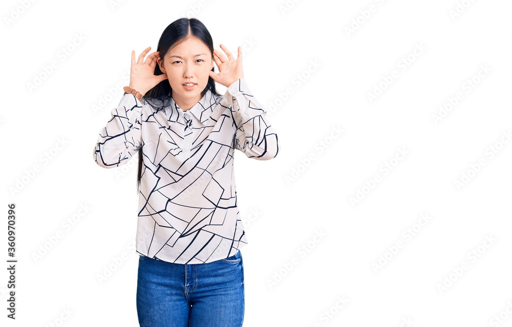 Young beautiful chinese woman wearing casual shirt trying to hear both hands on ear gesture, curious for gossip. hearing problem, deaf Young beautiful chinese woman wearing casual shirt trying to hear both hands on ear gesture, curious for gossip. hearing problem, deaf