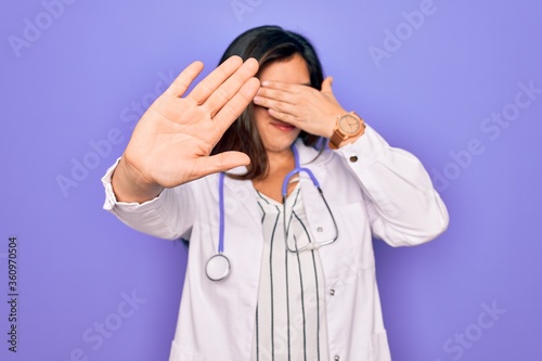 Professional doctor woman wearing stethoscope and medical coat over purple background covering eyes with hands and doing stop gesture with sad and fear expression. Embarrassed and negative concept.