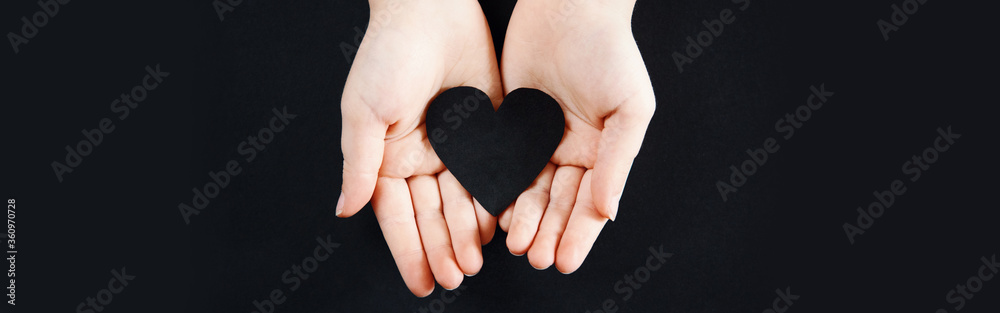 Obraz premium Human hands holding black paper heart on dark background. Support activist of USA movement black lives matter. Protest against racism. Web banner header for a website.