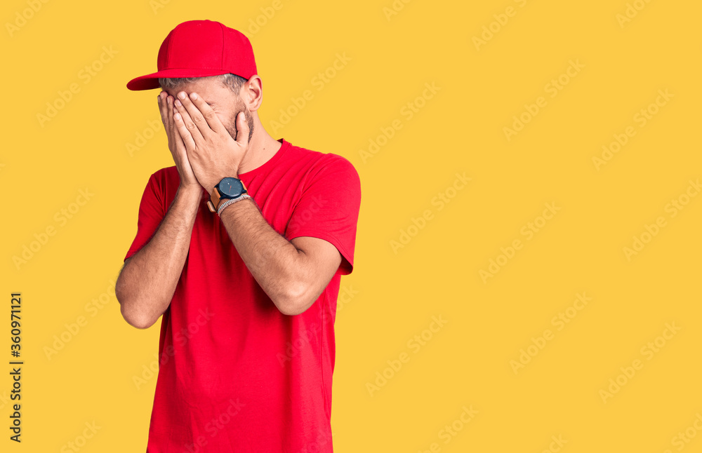 Young handsome blond man wearing t-shirt and cap with sad expression covering face with hands while crying. depression concept. Young handsome blond man wearing t-shirt and cap with sad expression covering face with hands while crying. depression concept.