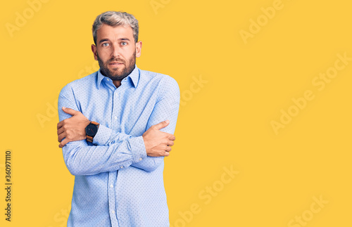 Young handsome blond man wearing elegant shirt shaking and freezing for winter cold with sad and shock expression on face © Krakenimages.com