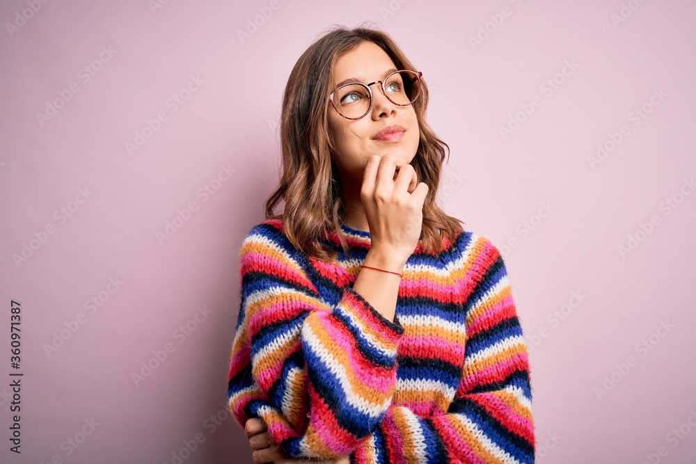 Young beautiful blonde girl wearing glasses and casual sweater over pink isolated background with hand on chin thinking about question, pensive expression. Smiling and thoughtful face. Doubt concept.
