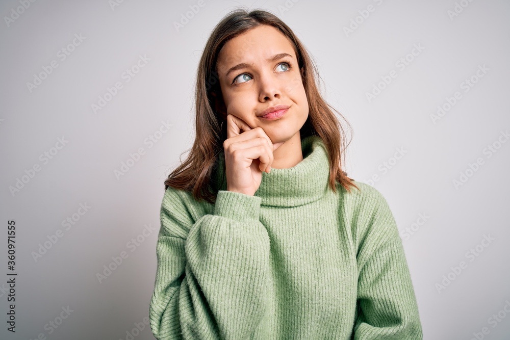 Young beautiful blonde girl wearing winter sweater standing over isolated background with hand on chin thinking about question, pensive expression. Smiling with thoughtful face. Doubt concept. Young beautiful blonde girl wearing winter sweater standing over isolated background with hand on chin thinking about question, pensive expression. Smiling with thoughtful face. Doubt concept.