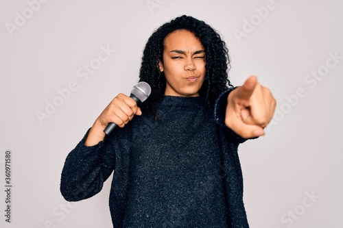 Young african american curly singer woman singing using microphone over white background pointing with finger to the camera and to you, hand sign, positive and confident gesture from the front