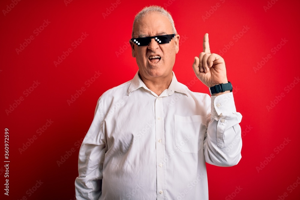 Middle age hoary man wearing funny sunglasses over isolated red background pointing finger up with successful idea. Exited and happy. Number one. Middle age hoary man wearing funny sunglasses over isolated red background pointing finger up with successful idea. Exited and happy. Number one.