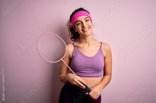 Beautiful sportswoman with curly hair wearing sportswear playing badminton uning racket with a happy face standing and smiling with a confident smile showing teeth photo