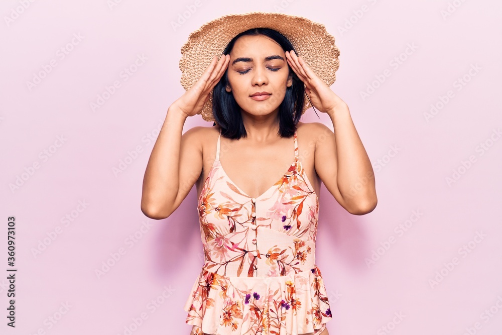 Young beautiful latin woman wearing summer hat with hand on head, headache because stress. suffering migraine.