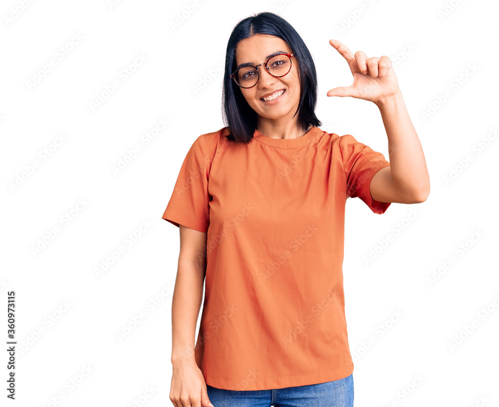 Young beautiful latin woman wearing casual clothes smiling and confident gesturing with hand doing small size sign with fingers looking and the camera. measure concept. Young beautiful latin woman wearing casual clothes smiling and confident gesturing with hand doing small size sign with fingers looking and the camera. measure concept.