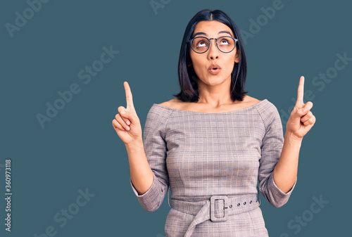 Young beautiful latin woman wearing casual clothes amazed and surprised looking up and pointing with fingers and raised arms.