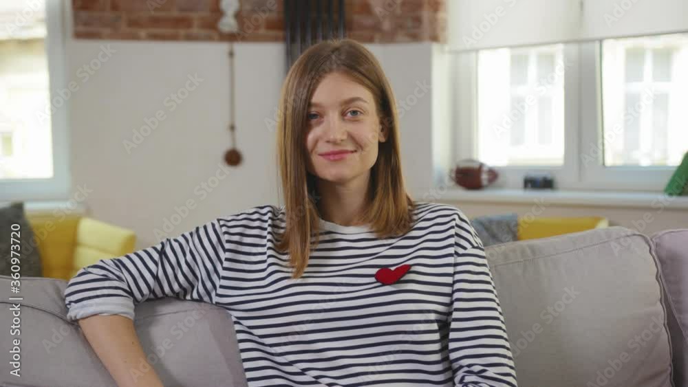 Portrait young woman sitting on couch using laptop looking at camera smiling at home chatting on computer media read network search room technology positive slow motion Portrait young woman sitting on couch using laptop looking at camera smiling at home chatting on computer media read network search room technology positive slow motion