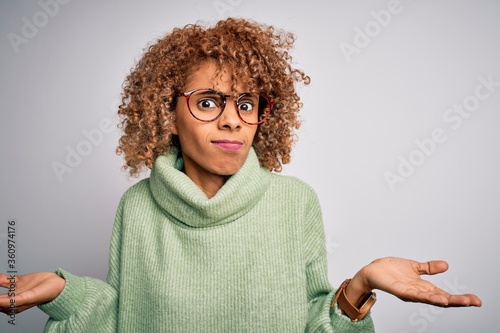 Young beautiful african american woman wearing turtleneck sweater and glasses clueless and confused with open arms, no idea concept.