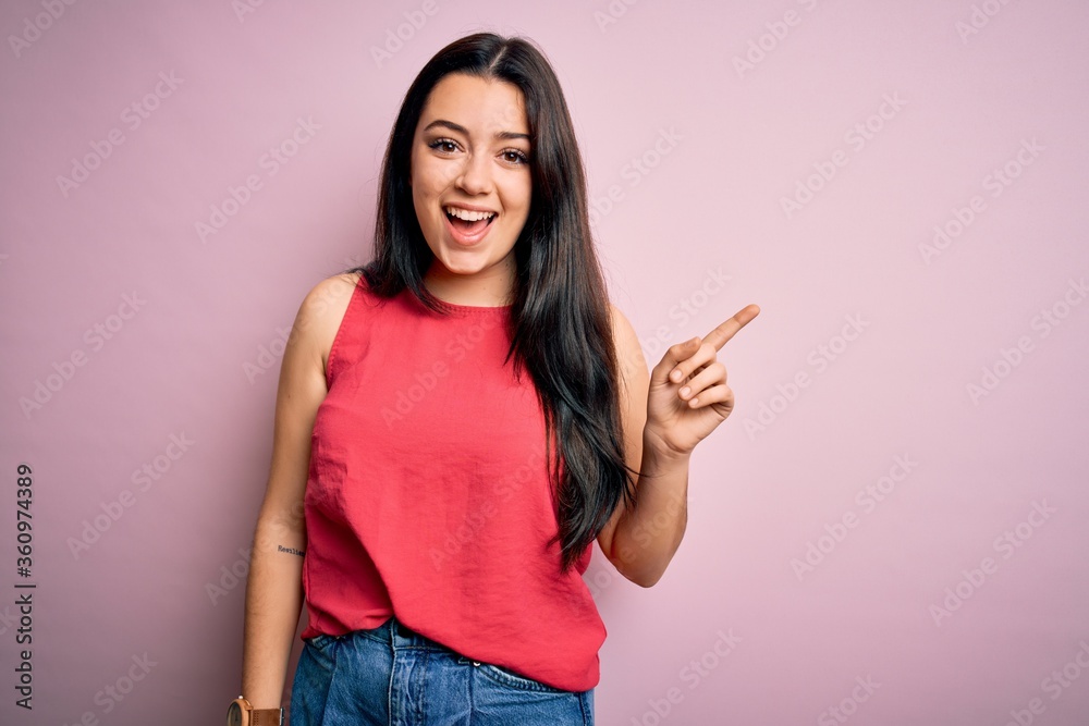 Young brunette woman wearing casual summer shirt over pink isolated background with a big smile on face, pointing with hand finger to the side looking at the camera. Young brunette woman wearing casual summer shirt over pink isolated background with a big smile on face, pointing with hand finger to the side looking at the camera.
