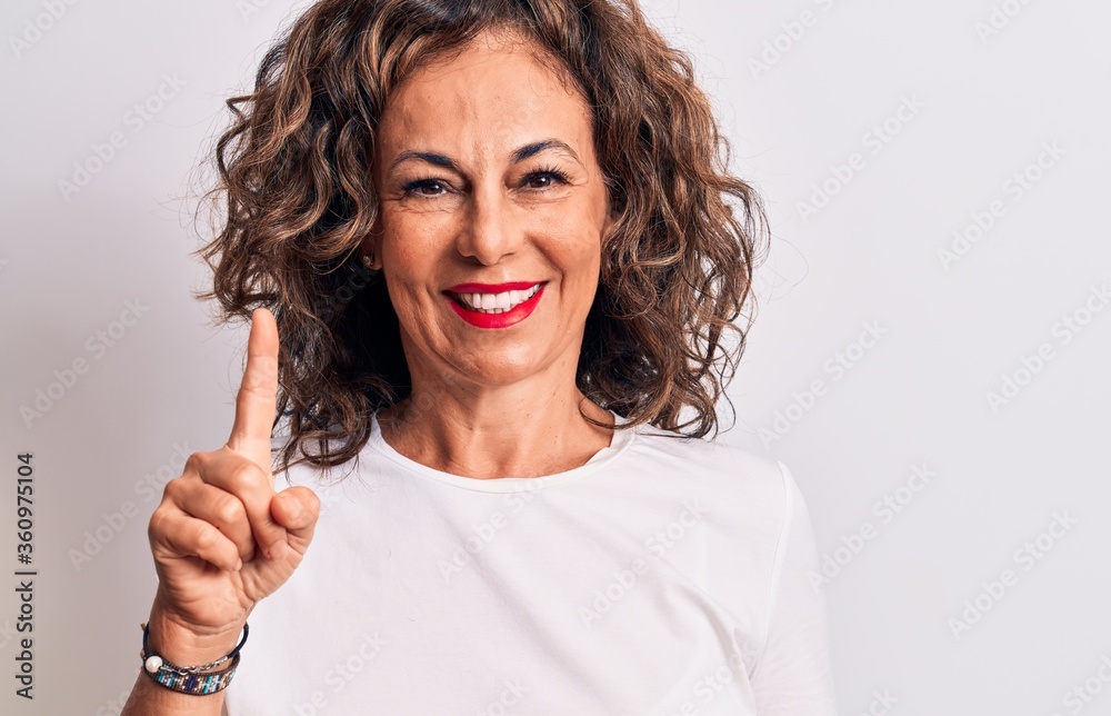 Middle age beautiful brunette woman wearing casual t-shirt standing over white background smiling with an idea or question pointing finger up with happy face, number one