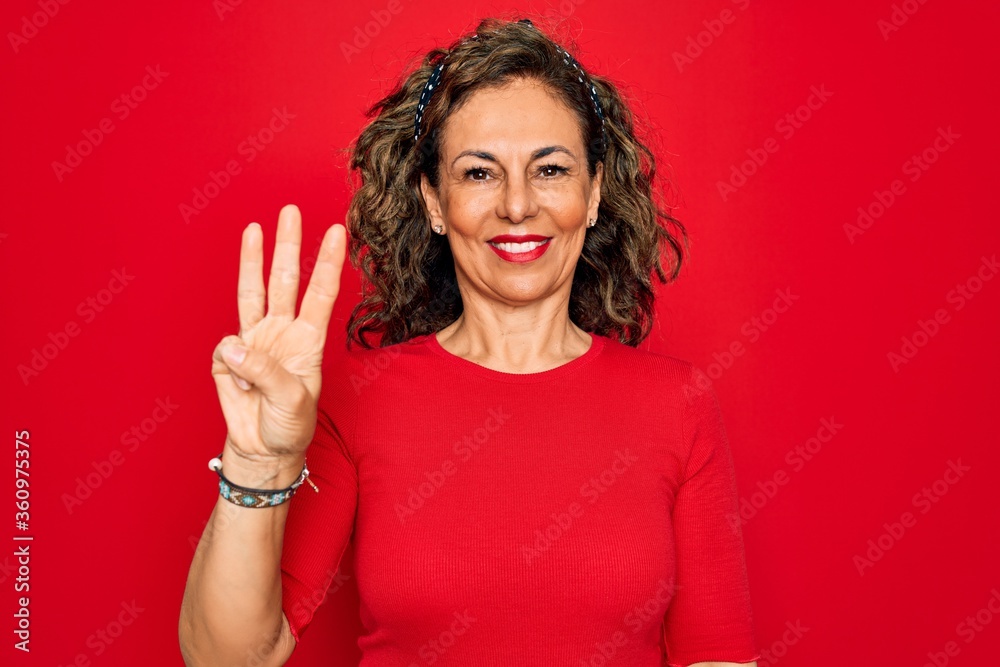 Middle age senior brunette woman wearing casual t-shirt standing over red background showing and pointing up with fingers number three while smiling confident and happy.