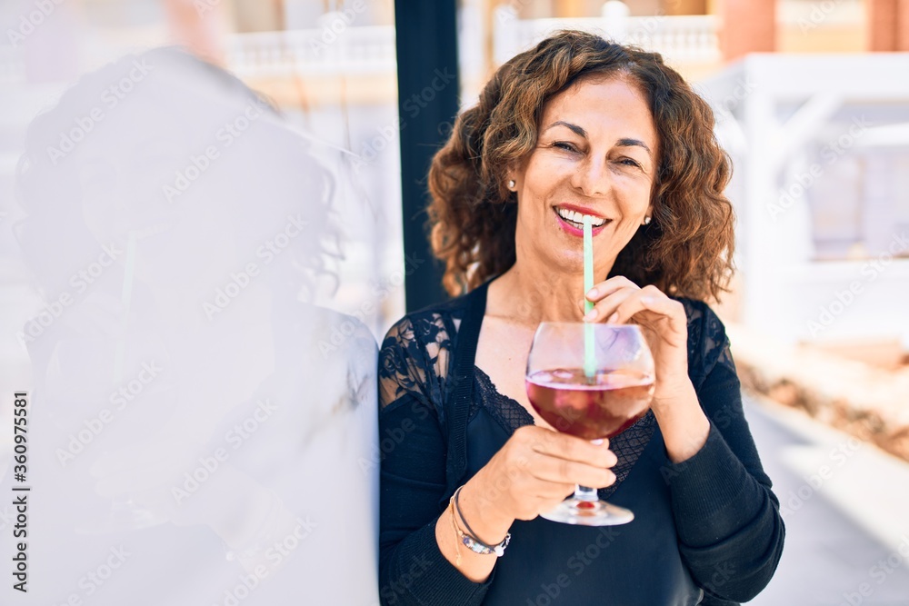 Middle age beautiful brunette woman smiling happy and confident. Leaning on the wall with smile on face drinking cup of sangria at the terrace restaurant Middle age beautiful brunette woman smiling happy and confident. Leaning on the wall with smile on face drinking cup of sangria at the terrace restaurant