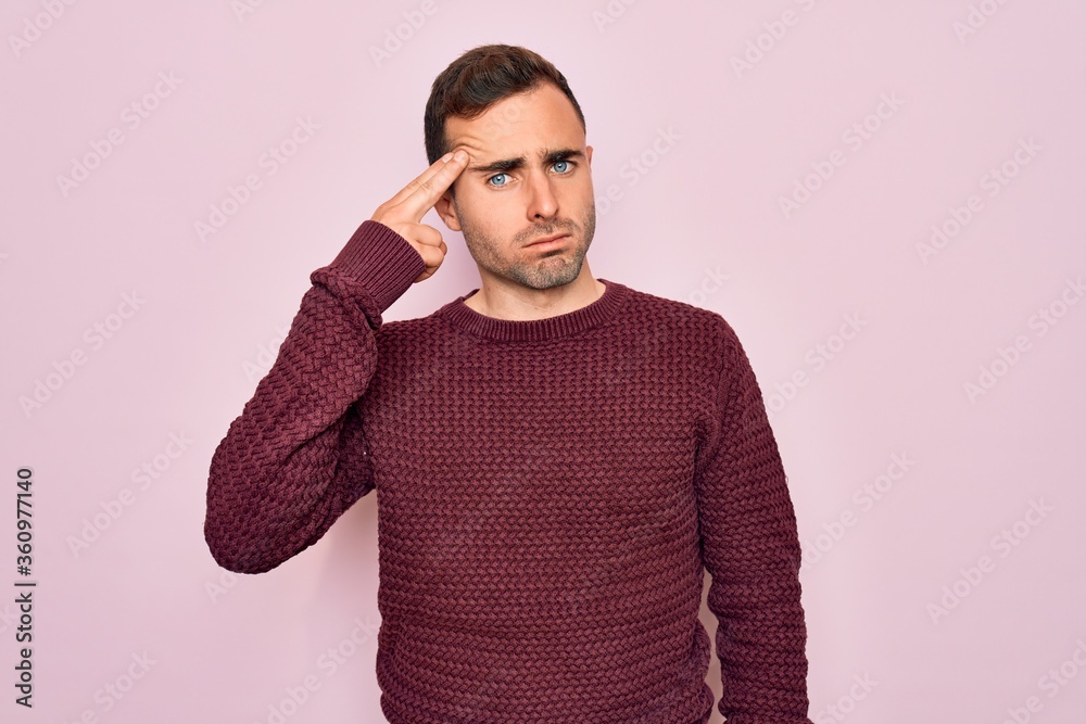 Young handsome man with blue eyes wearing casual sweater standing over pink background Shooting and killing oneself pointing hand and fingers to head like gun, suicide gesture. Young handsome man with blue eyes wearing casual sweater standing over pink background Shooting and killing oneself pointing hand and fingers to head like gun, suicide gesture.
