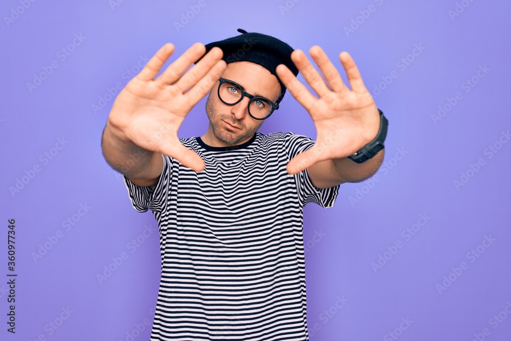 Fototapeta premium Handsome man with blue eyes wearing striped t-shirt and french beret over purple background doing frame using hands palms and fingers, camera perspective
