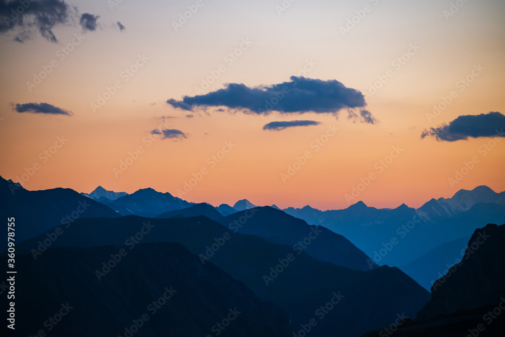 Colorful dawn landscape with beautiful mountains silhouettes and golden gradient sky with blue clouds. Vivid mountain scenery with picturesque multicolor sunset. Scenic sunrise view to mountain range.