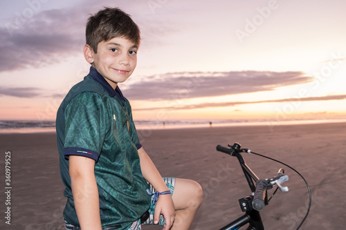 Retrato de garoto sentado na bicicleta em final de tarde na praia  photo