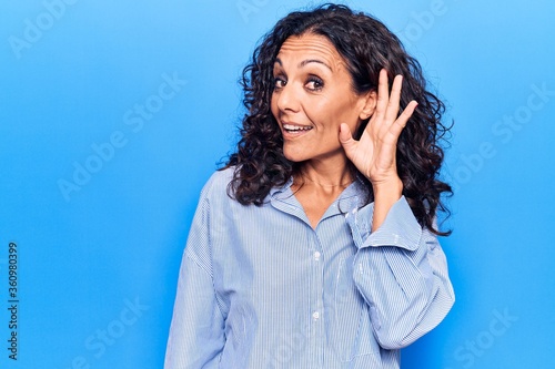 Middle age beautiful woman wearing casual shirt smiling with hand over ear listening and hearing to rumor or gossip. deafness concept.