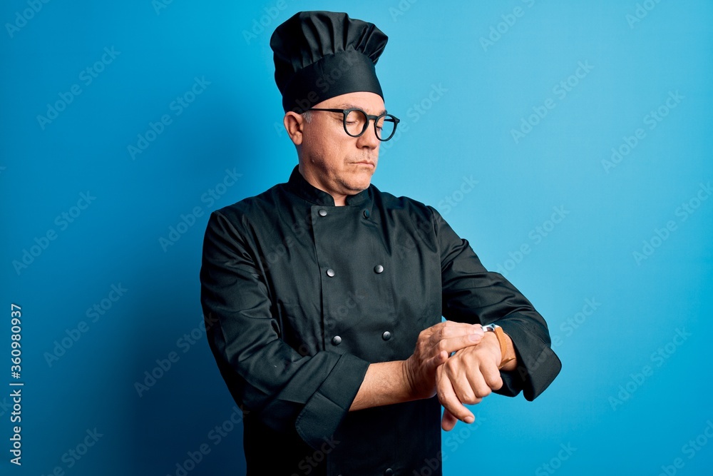Middle age handsome grey-haired chef man wearing cooker uniform and hat Checking the time on wrist watch, relaxed and confident