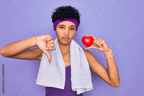 Beautiful african american afro sporty woman doing exercise wearing towel holding heart with angry face  negative sign showing dislike with thumbs down  rejection concept