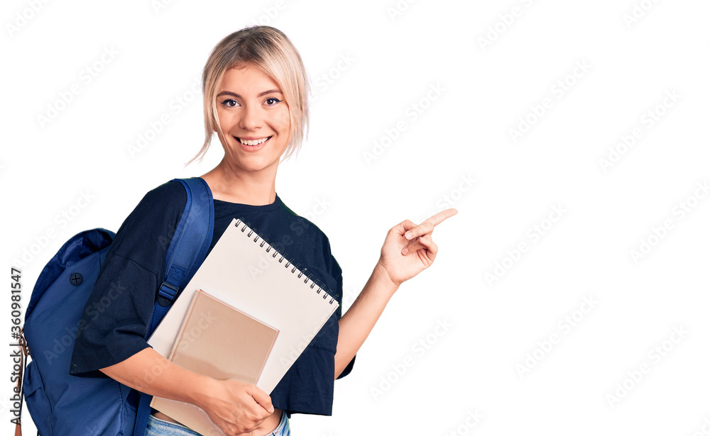 Young beautiful blonde woman wearing student backpack holding notebook smiling happy pointing with hand and finger to the side Young beautiful blonde woman wearing student backpack holding notebook smiling happy pointing with hand and finger to the side