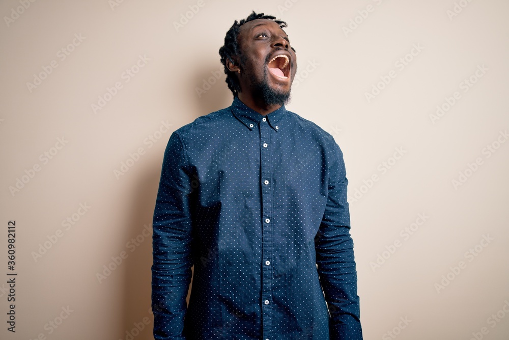 Obraz premium Young handsome african american man wearing casual shirt standing over white background angry and mad screaming frustrated and furious, shouting with anger. Rage and aggressive concept.