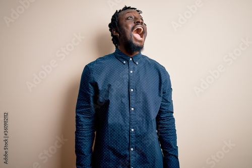 Young handsome african american man wearing casual shirt standing over white background angry and mad screaming frustrated and furious, shouting with anger. Rage and aggressive concept.