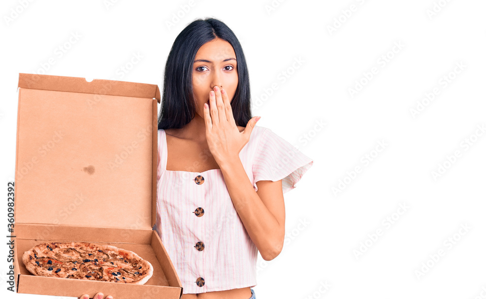 Young beautiful latin girl holding delivery pizza box covering mouth with hand, shocked and afraid for mistake. surprised expression Young beautiful latin girl holding delivery pizza box covering mouth with hand, shocked and afraid for mistake. surprised expression