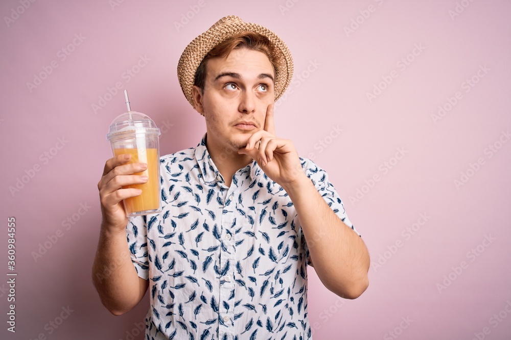 Young handsome redhead man on vacation drinking glass of healthy orange juice serious face thinking about question with hand on chin, thoughtful about confusing idea Young handsome redhead man on vacation drinking glass of healthy orange juice serious face thinking about question with hand on chin, thoughtful about confusing idea