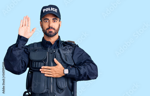 Young hispanic man wearing police uniform swearing with hand on chest and open palm, making a loyalty promise oath