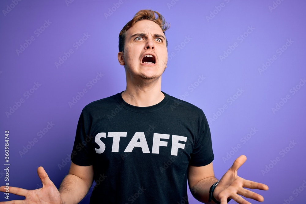 Young handsome redhead worker man wearing staff t-shirt uniform over purple background crazy and mad shouting and yelling with aggressive expression and arms raised. Frustration concept. Young handsome redhead worker man wearing staff t-shirt uniform over purple background crazy and mad shouting and yelling with aggressive expression and arms raised. Frustration concept.