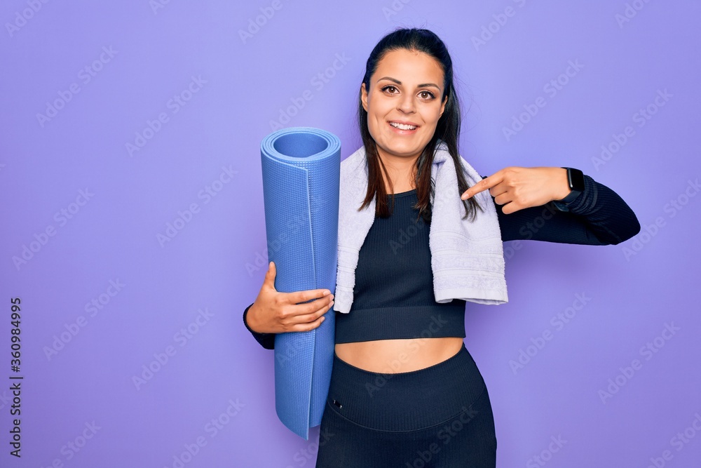 Young beautiful brunette sporty woman using sport towel hoding mat to do yoga pointing finger to one self smiling happy and proud